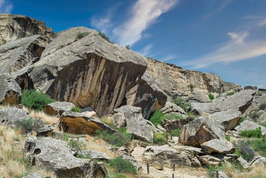 A view of the rocky landscape in Qobustan, Azerbaijan, with a path winding through the large boulders and green vegetation.