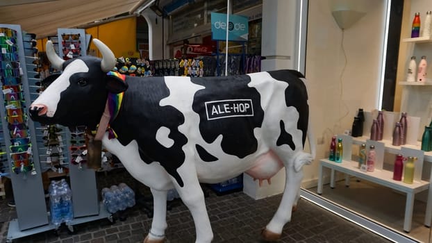Rimini, Italy - June 25, 2024: A black and white cow in front of the Ale-hop store with a rainbow flag around its neck at Rimini, Italy
