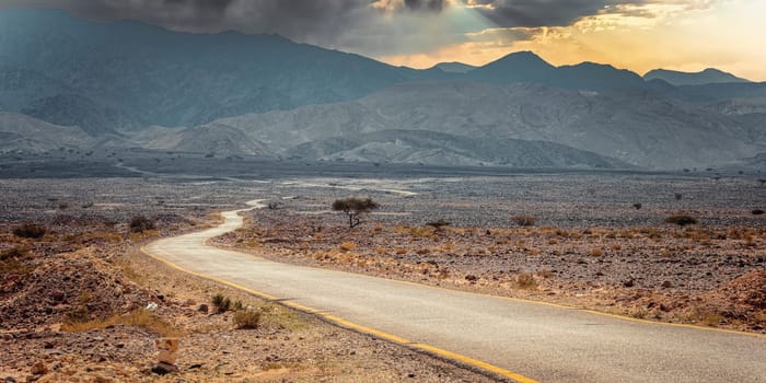 Empty asphalt road dramatic desert landscape mountains and clouds