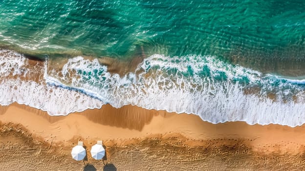 Aerial view of a pristine sandy beach meeting turquoise water with gentle waves lapping the shore, two beach umbrellas provide a splash of white against the golden sand