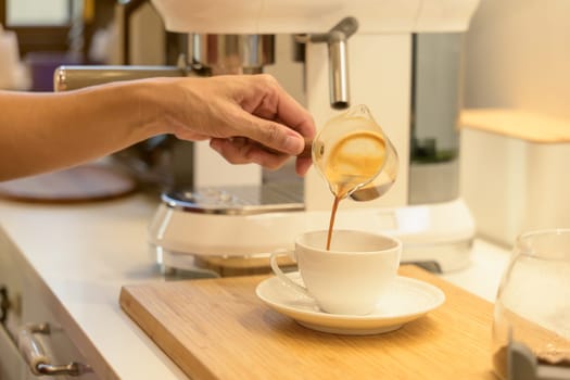 Woman hand pouring fresh hot espresso coffee into a white cup in the kitchen at home in the morning
