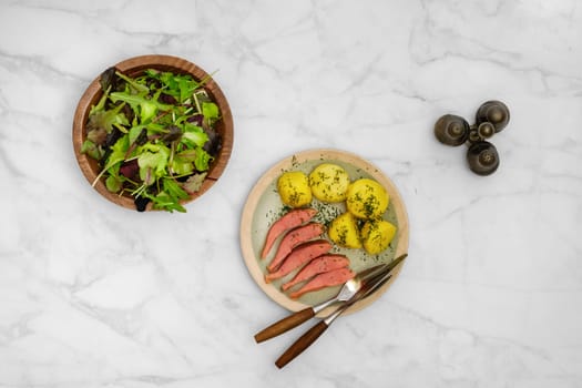Top view of a rustic meal consisting of fresh green salad, hot smoked humpback salmon and boiled potatoes seasoned with herbs, served on a marble table