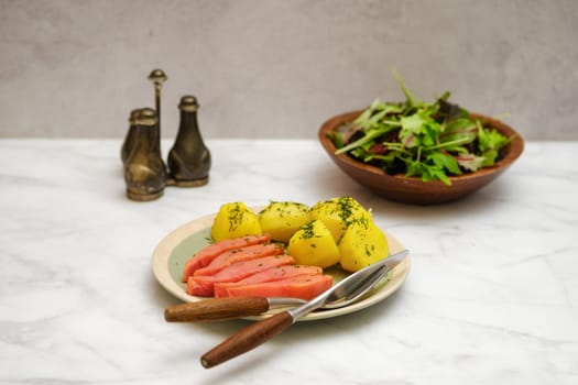 Hot smoked humpback salmon and boiled potatoes with fresh green salad on a marble table