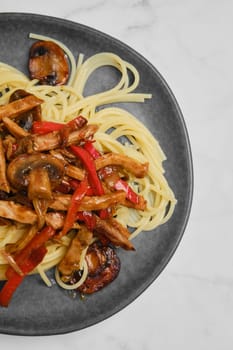Closeup view of a plate with spaghetti with mushrooms, bell pepper and pork