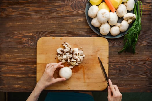 Unrecognizable woman chopping champignon mushrooms, top view