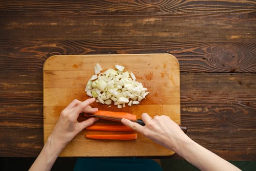 Unrecognizable woman cut carrot on a quarters with a knife, top view