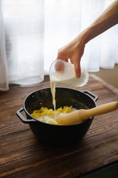 Hand of woman pouring milk into saucepan with mashed potatoes