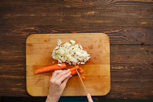 Unrecognizable woman chopping carrot on cutting board with a knife, top view