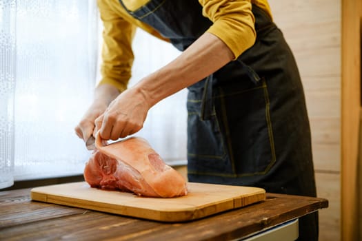 Unrecognizable man in apron cuts off skin from raw pork shoulder