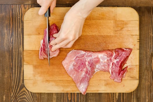 Top view of hands of unrecognizable man slicing pork shoulder on wooden cutting board