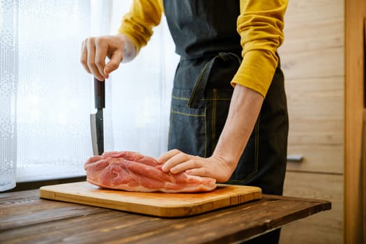 Unrecognizable man in the kitchen leans with one hand on a pork shoulder and with the other hand on a sharp knife