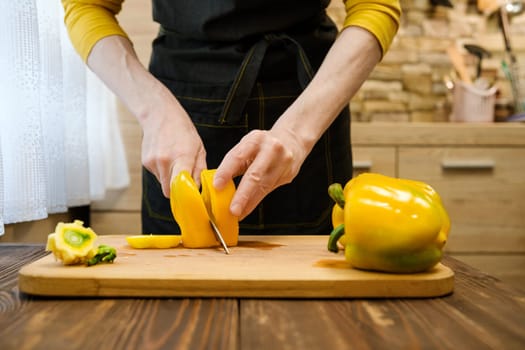 Unrecognizable man cutting on half bell peppers on wooden cutting board
