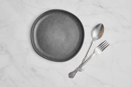 top view of empty ceramic plate and spoon with fork on marble background