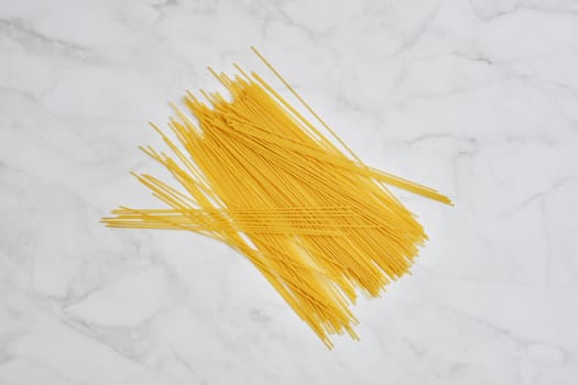 Top view of raw spaghetti scattered on marble background