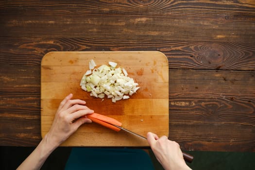 Unrecognizable woman cut carrot on a half with a knife, top view