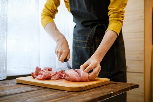 Unrecognizable man cuts pork meat into large pieces in the kitchen
