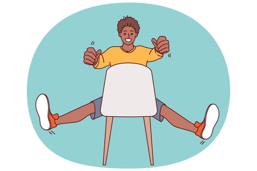 Man sitting on chair holds invisible car steering wheel in hands and imagines that is driving on high-speed road working as taxi driver. African american teenager guy drives invisible car