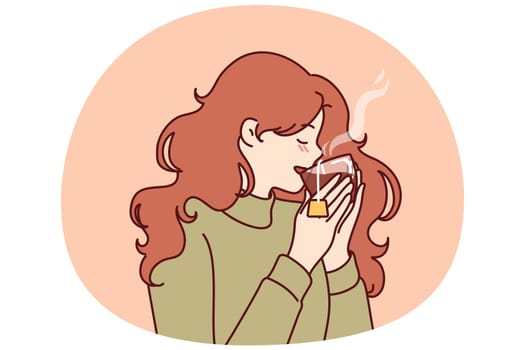 Woman drinks hot tea from transparent glass, enjoying taste of warming drink in cold winter weather. Young girl in sweater feels cozy and drinks tea drink take break to rest from work