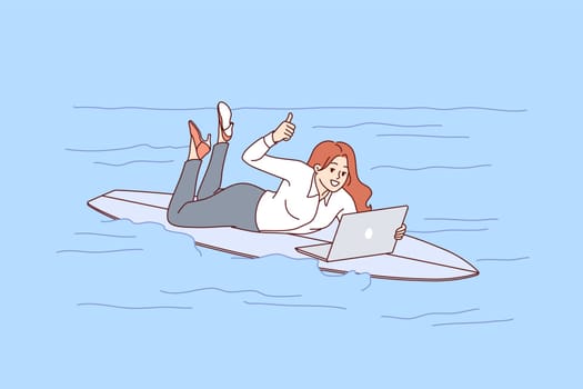Woman freelancer rides surfboard on sea and works with laptop, showing thumbs up. Busy girl freelancer in casual clothes jobs during vacation due to lack of time management skills.