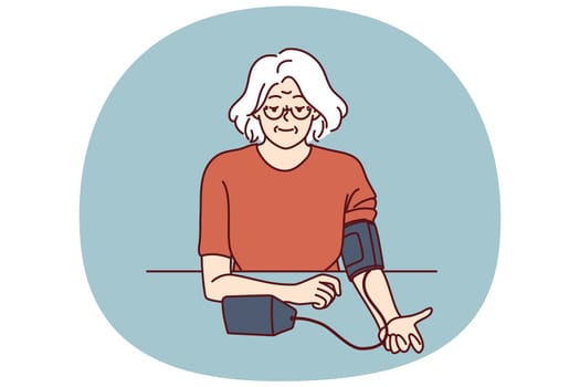 Elderly woman uses tonometer to measure blood pressure and check for symptoms of hypertension. Gray-haired grandmother independently measures blood pressure, taking care of own health