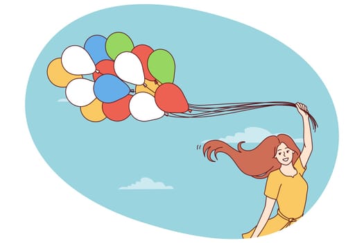 Happy young woman with balloons rejoices at onset of spring and warm weather standing on background of blue sky. Cheerful girl in summer dress with balloons symbolizing lightness and good mood