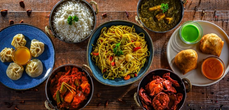 Composition with indian dishes: samosa, pakora, palak paneer, jalfrezi, thukpa and naan bread