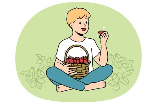 Little boy eats strawberries sitting in clearing with yagid bushes on fruit farm or plantation. Child enjoys taste of fresh organic strawberries grown without use of pesticides and chemicals.
