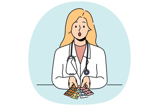 Surprised woman doctor with pills in blisters feels distrustful of drugs that can harm patient. Skeptical girl doctor with stethoscope around neck does not want to recommend untested medicines