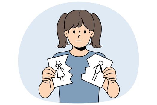 Sad little girl is nervous about parents divorce and is holding torn drawing of mom and dad. Sad child suffers after learning about dissolution of marriage between mother and father
