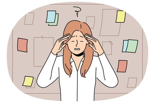 Tired businesswoman stands near blackboard with notes and grabs head after learning about overdue deadline. Woman manager feeling headache due to regular overtime caused by strict deadline
