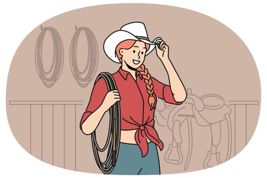 Woman jockey stands in stable wearing cowboy hat and holding long rope waiting for horses to appear. Girl rancher dressed in cowgirl style smiling when you cheer for jockey at races