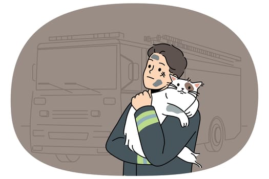 Man firefighter with cat heroically rescued from burning house stands near fire truck and hugs pet. Brave guy in uniform of firefighter or rescue worker helped cat get out of trouble