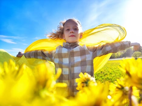 A young girl stands joyfully with arms outstretched, embracing the sunshine and a bright yellow scarf against a backdrop of flowers.