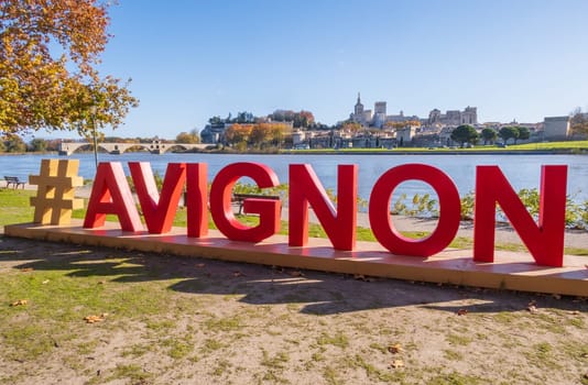Avignon, France - November 25 2023: Avignon city and his famous bridge photographed with red letters of Avignon sign in the foreground.  Medieval Papal city on the Rhone River