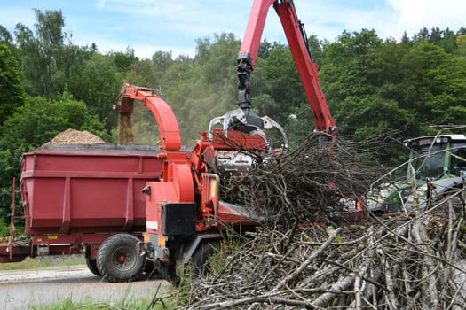 A wood chipper chops up branches in the forest. The chopped wood is used as silage in animal feed or biogas plants. A gripper arm places the remaining wood on the conveyor belt