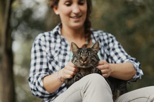 Smiling woman with braided curly hair and checkered shirt holds a relaxed tabby cat. The cat’s face shows pure bliss, akin to a spa session for felines