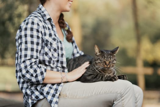 Woman with curly hair and a checkered shirt beams while holding a relaxed tabby cat. The cat’s expression reflects immense satisfaction, as if indulging in a spa treatment