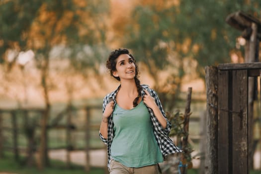 Curly-haired woman with a braid and checkered shirt smiles brightly while walking outside. Her cheerful demeanor and relaxed stance highlight a serene and pleasant environment