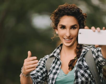 Curly-haired woman with a braid and checkered shirt smiles brightly while directing a photo with her smartphone. Her cheerful demeanor and focused posture highlight her enthusiasm for photography