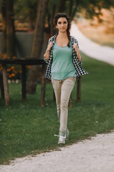 Woman with curly hair in a braid, wearing a checkered shirt and green top, walks outside with a bright smile. Her relaxed demeanor reflects a peaceful and joyful environment