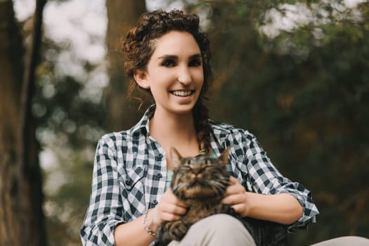 young woman with curly hair and a checkered shirt holds a very content tabby cat. Both appear happy, with the cat looking like it's enjoying a spa experience