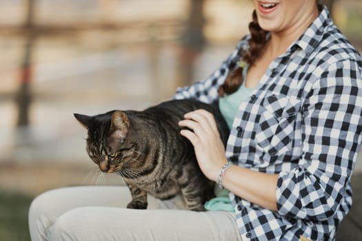 woman in a checkered shirt with curly hair holds a blissful tabby cat. The cat’s serene expression suggests it is enjoying a luxurious spa experience