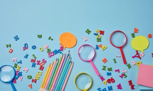 Stationery laid out on a blue background. Multi-colored  sticky notes and wooden letters, preparing for study or work, organizing workspace