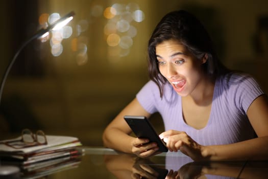 Amazed woman checking phone content in the night at home