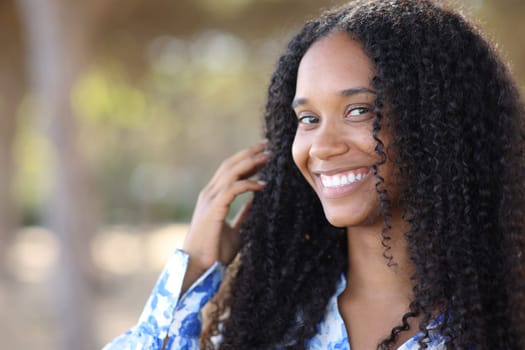 Black woman with white smile looking at you in a park