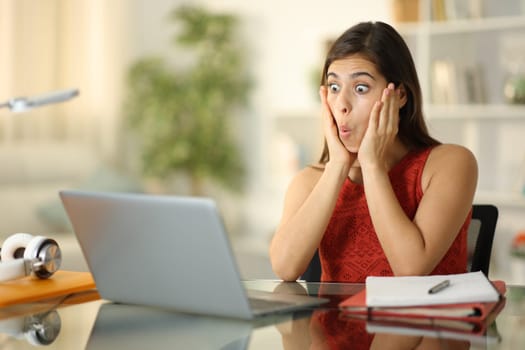 Amazed student checking laptop content sitting at home