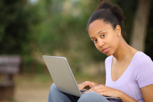 Serious black woman using laptop posing lookking at camera in a park