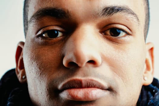 Close-up of a young man with short hair, dark complexion, and earrings in both ears. His serious expression is highlighted by the focused gaze of his dark, almond-shaped eyes