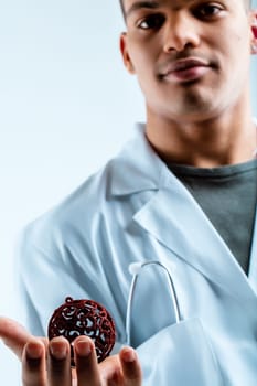 Military doctor with a gentle smile, holding a red Christmas ornament. Wearing a white lab coat, he aims to improve the health of his patients during the holiday season