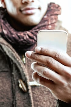 unrecognizable man with a warm smile, holding a smartphone with both hands. Dressed in a grey coat and scarf, he seems to be enjoying a moment of connection and interaction